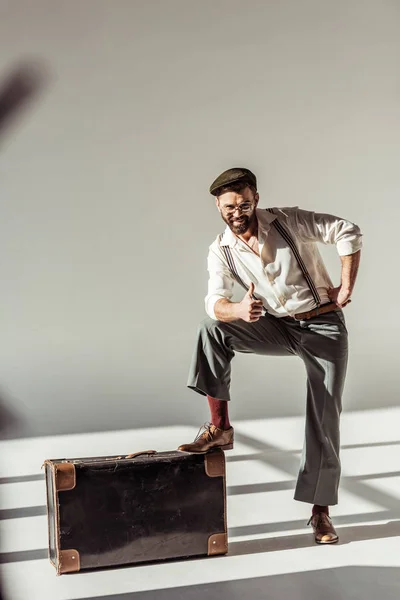 Bearded man with vintage suitcase showing thumb up and looking at camera on grey background — Stock Photo