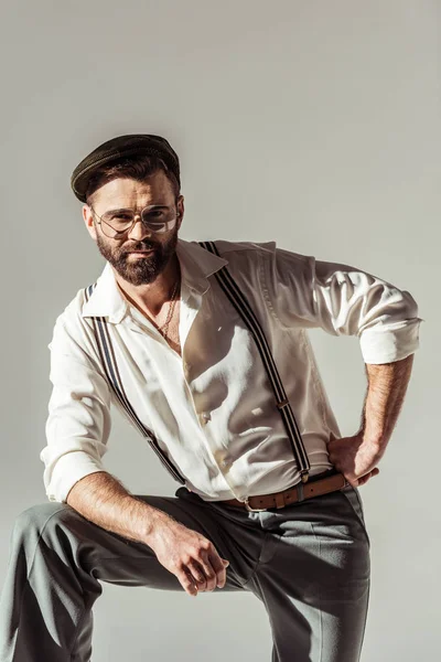 Bärtiger, stylischer Mann mit Mütze blickt vereinzelt in die Kamera auf grau — Stockfoto
