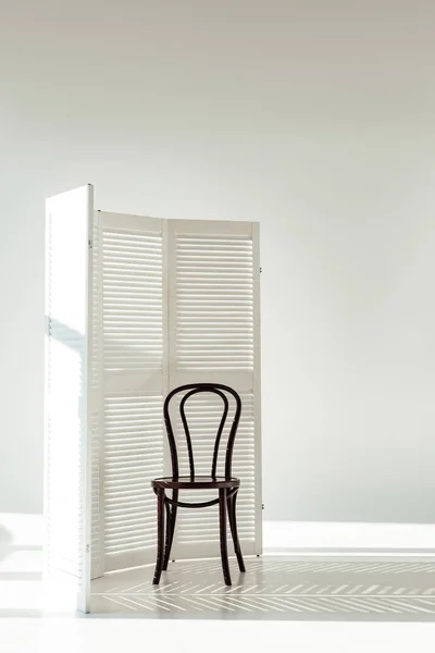 Dark wooden chair and white room divider with shadows and sunlight — Stock Photo