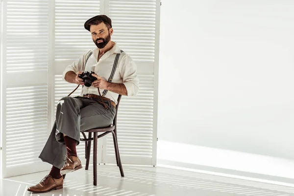 Bearded stylish man sitting on chair with vintage film camera — Stock Photo