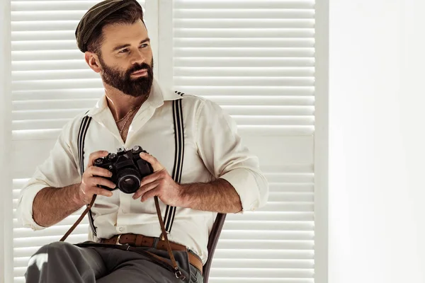 Schöner bärtiger Mann sitzt auf Stuhl und hält alte Filmkamera — Stockfoto