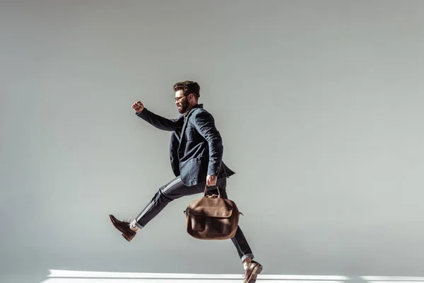 Hombre barbudo con bolsa marrón saltando sobre fondo gris - foto de stock