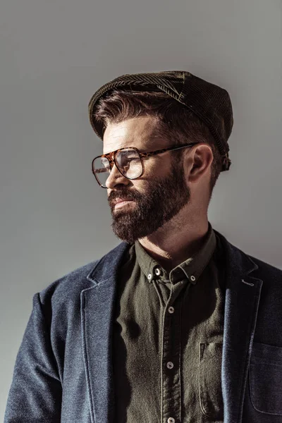 Nahaufnahme eines gutaussehenden bärtigen Mannes mit Brille und Mütze isoliert auf grau — Stockfoto