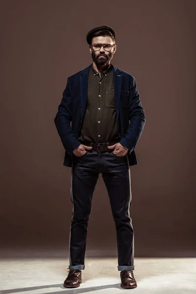 Красивый бородатый мужчина с руками в кармане, смотрящий на камеру на коричневом фоне — стоковое фото