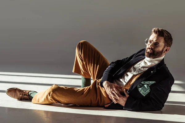 Handsome bearded man in glasses with clenched hands lying on floor — Stock Photo