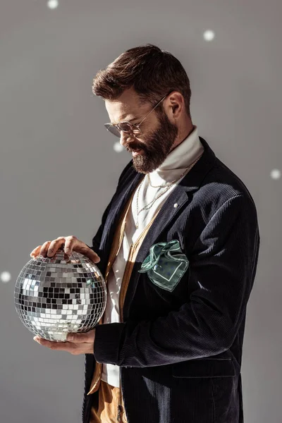 Bel homme barbu dans des lunettes tenant boule disco sur fond gris — Photo de stock