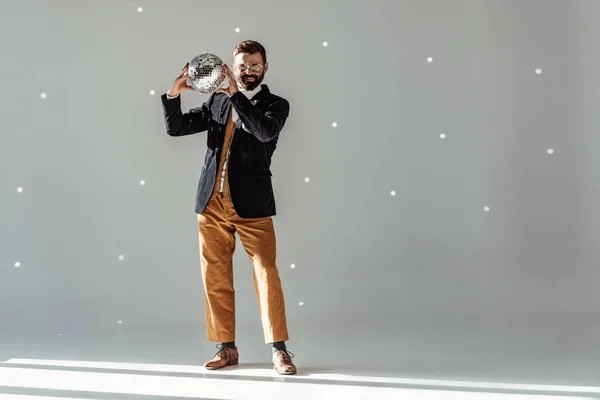 Handsome man holding disco ball, smiling and looking at camera on grey background — Stock Photo