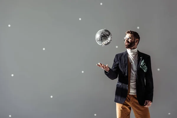 Красивый мужчина в очках бросает диско мяч на сером фоне — стоковое фото