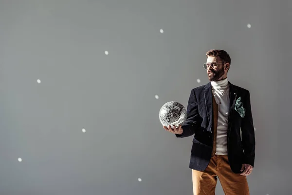 Bärtiger Mann blickt auf Mosaik-Discokugel in der Hand auf grauem Hintergrund — Stockfoto