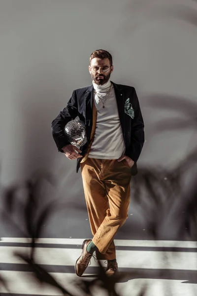 Selective focus of bearded man holding mosaic disco ball and looking at camera on grey background — Stock Photo