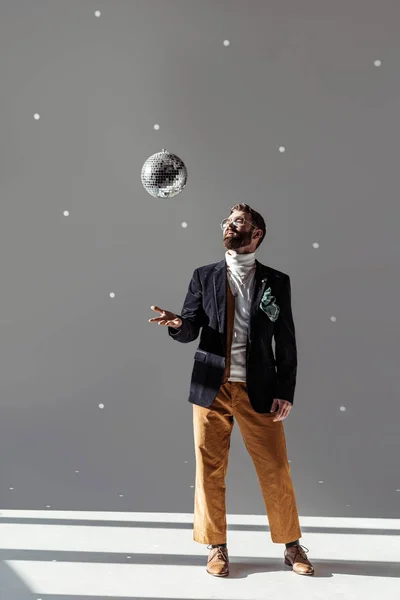 Handsome man in glasses high throwing up disco ball on grey background — Stock Photo