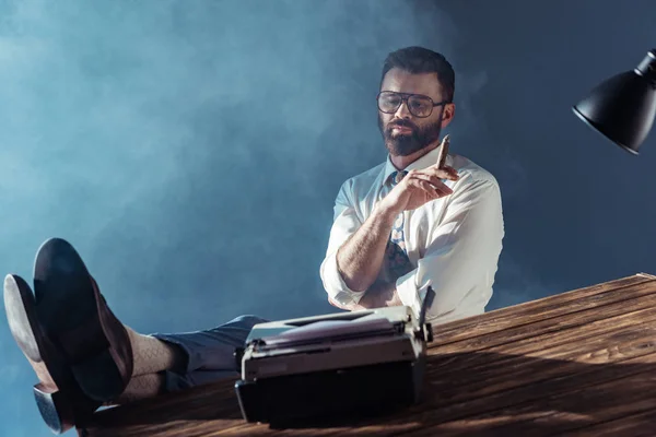 Hombre guapo fumando y sentado en silla cerca de la mesa - foto de stock