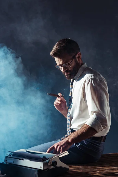 Schöner rauchender Mann sitzt auf Tisch mit Schreibmaschine — Stockfoto