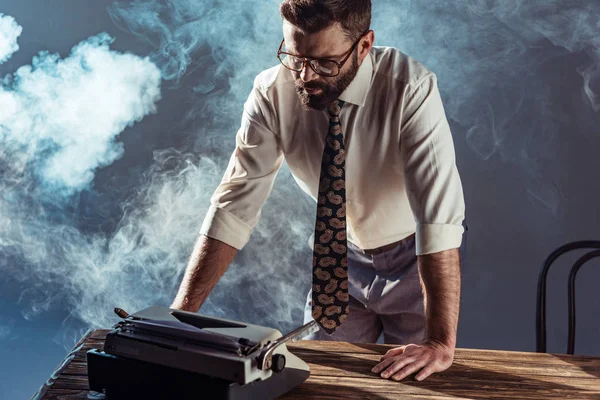 Bel homme barbu tenant cigare et regardant la machine à écrire — Photo de stock