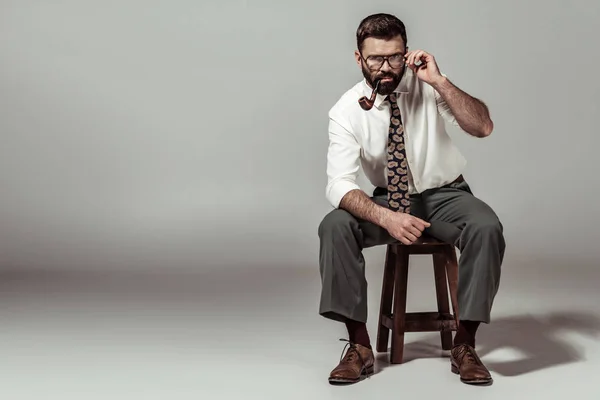 Красивый бородатый мужчина в очках сидит на стуле и трогает очки — стоковое фото
