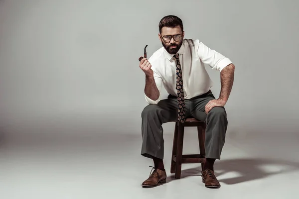 Bel homme barbu en lunettes et chemise assis sur une chaise avec tuyau — Photo de stock