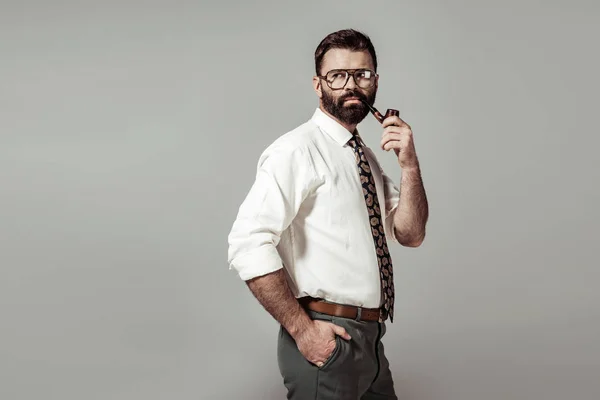 Bello uomo barbuto in occhiali mettendo mano in tasca e fumare isolato su grigio — Foto stock
