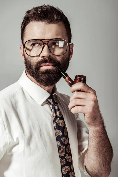 Bell'uomo barbuto in occhiali, camicia e cravatta smoking pipe isolato su grigio — Foto stock