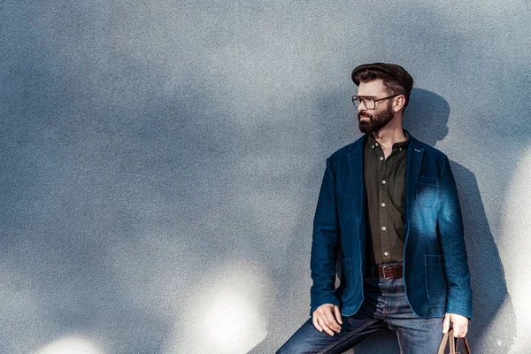 Handsome bearded man in glasses and cap standing near wall — Stock Photo