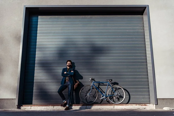 Красивый бородатый мужчина в очках и кепке позирует рядом с велосипедом — стоковое фото