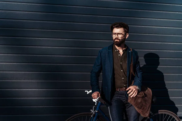 Hombre barbudo guapo en gafas y gorra bolsa de sujeción y bicicleta - foto de stock