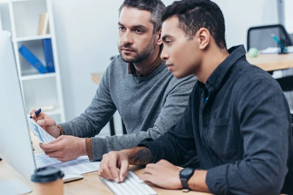 Fokussierte Mitarbeiter, die im Büro mit Papieren und Desktop-Computern arbeiten — Stockfoto