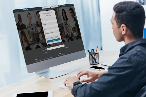Jovem empresário usando computador desktop com site linkedin na tela no escritório — Fotografia de Stock