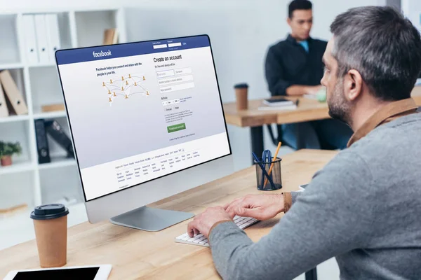 Hombre de negocios que usa computadora de escritorio con el sitio web de facebook en la pantalla en la oficina - foto de stock