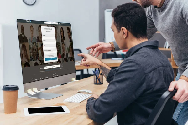 Recortado de colegas de negocios utilizando ordenador de sobremesa con linkedin sitio web en la pantalla en la oficina - foto de stock