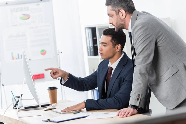 Focused businessmen pointing with finger and looking at desktop computer in office — Stock Photo