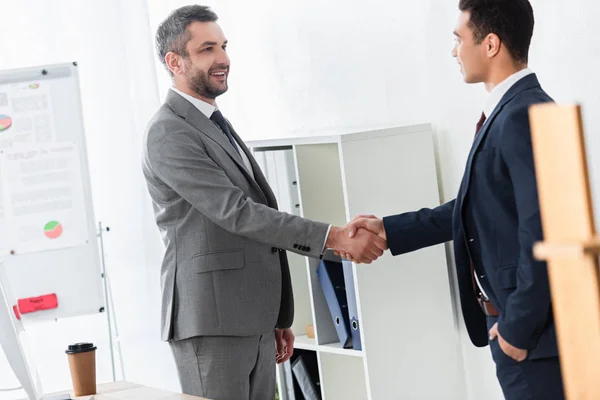 Homem de negócios feliz em formal desgaste apertando as mãos e sorrindo uns aos outros no escritório — Fotografia de Stock