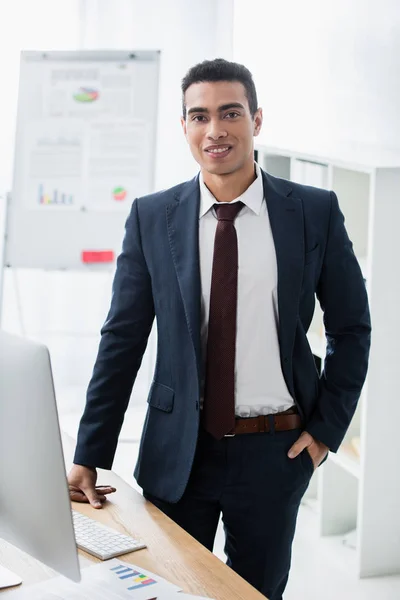 Schöner junger Geschäftsmann, der mit der Hand in der Tasche im Büro in die Kamera lächelt — Stockfoto