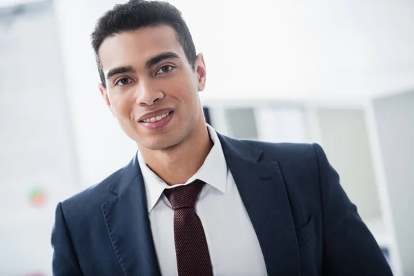 Porträt eines hübschen jungen gemischten Geschäftsmannes, der in die Kamera lächelt — Stockfoto