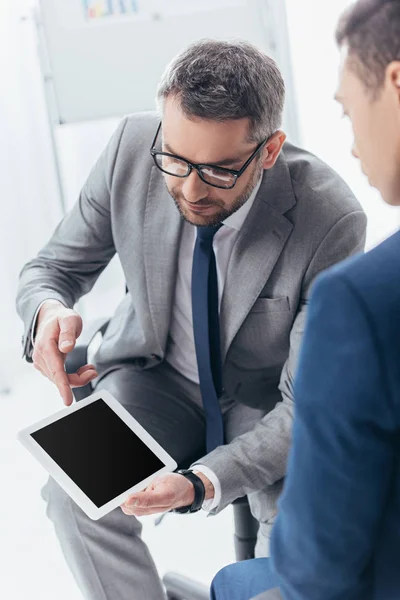 Cropped shot of businessman in eyeglasses showing digital tablet with blank screen to male colleague in office — Stock Photo