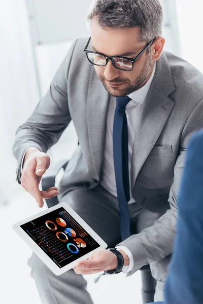 Hochwinkelaufnahme eines gutaussehenden Geschäftsmannes in Brille mittels digitalem Tablet mit Geschäftsdiagrammen und Grafiken — Stockfoto