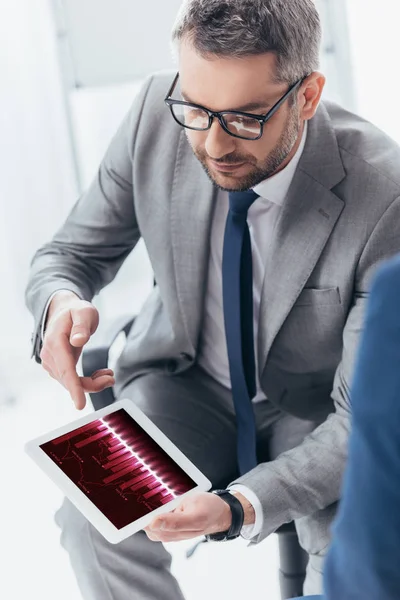 Vista de ángulo alto de hombre de negocios guapo en gafas usando tableta digital con gráficos de negocios - foto de stock