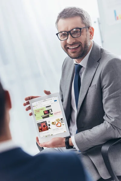 Lächelnder Geschäftsmann mit Brille und digitalem Tablet mit Ebay-Anwendung auf dem Bildschirm — Stockfoto