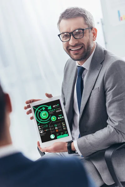 Smiling businessman in eyeglasses holding digital tablet with charts and graphs on screen — Stock Photo