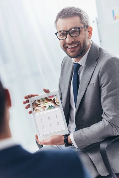 Улыбающийся бизнесмен в очках держит цифровой планшет с четырехквадратным приложением на экране — стоковое фото