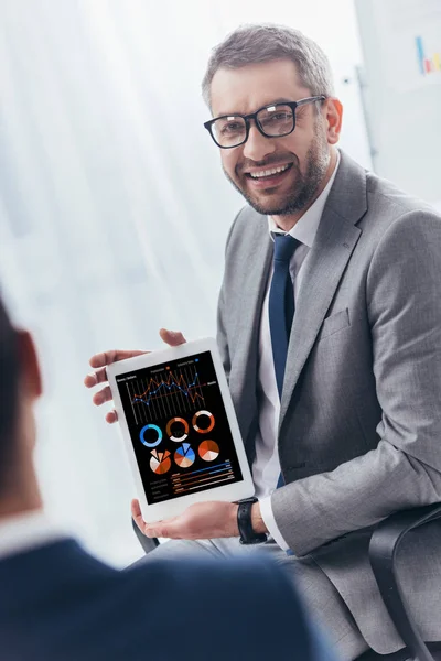 Homem de negócios sorridente em óculos segurando tablet digital com gráficos e gráficos na tela — Fotografia de Stock