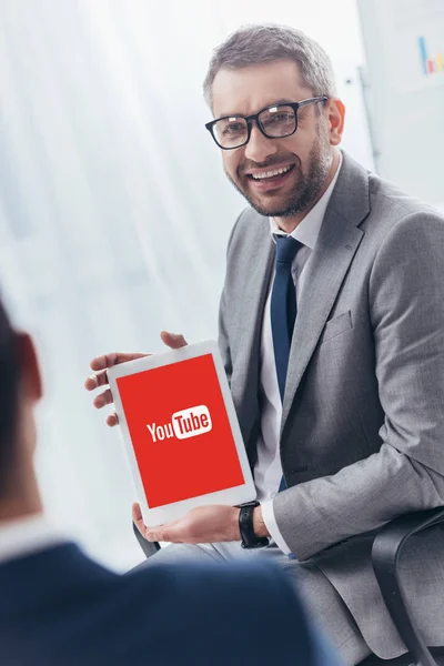 Smiling businessman in eyeglasses holding digital tablet with youtube app on screen — Stock Photo