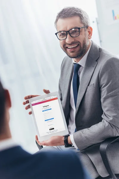 Homem de negócios sorridente em óculos segurando tablet digital com aplicativo instagram na tela — Fotografia de Stock