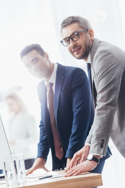 Hommes d'affaires professionnels penchés à table et souriant à la caméra dans le bureau — Photo de stock