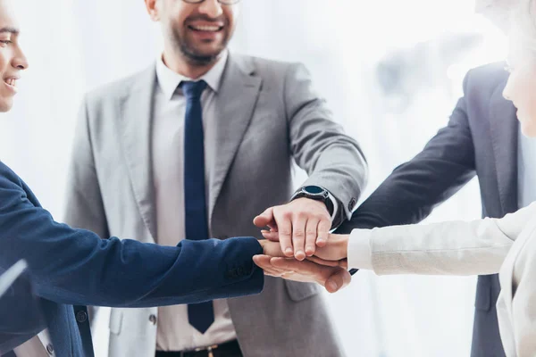 Recortado disparo de feliz equipo de negocios apilando manos en la oficina - foto de stock