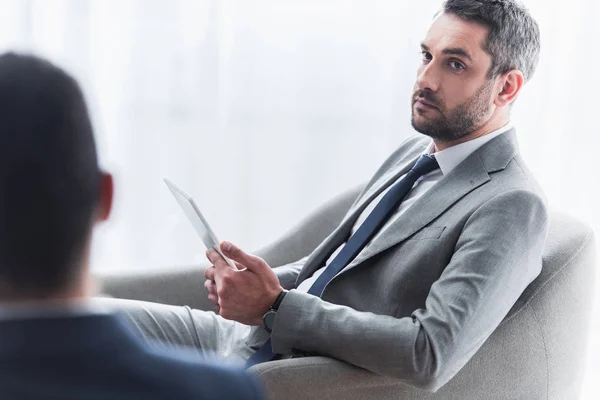 Recortado disparo de empresario serio sosteniendo tableta digital y mirando a colega masculino en primer plano - foto de stock