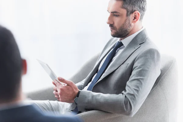 Hombre de negocios barbudo serio sentado y usando tableta digital en la oficina - foto de stock