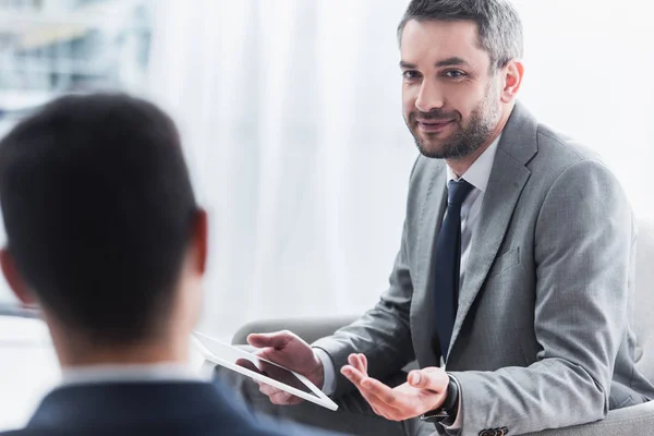 Smiling bearded businessman holding digital tablet and looking at male colleague on foreground — Stock Photo