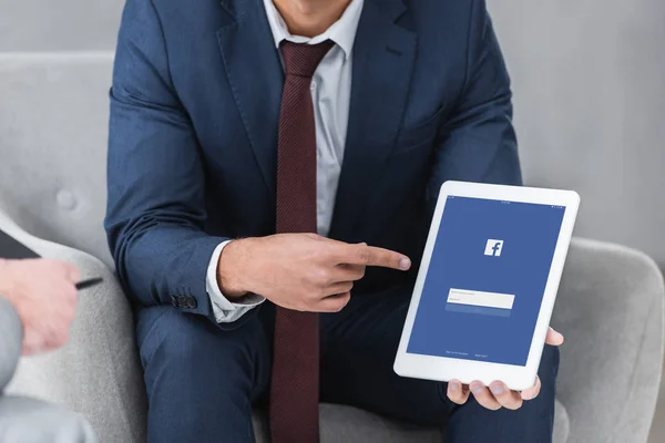 Cropped shot of businessman in formal wear pointing with finger at digital tablet with facebook app — Stock Photo