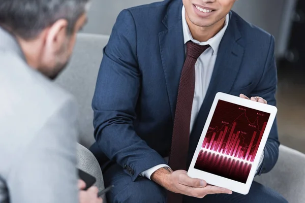 Schnappschuss eines lächelnden jungen Geschäftsmannes, der einem Kollegen ein digitales Tablet mit Geschäftsdiagrammen zeigt — Stockfoto