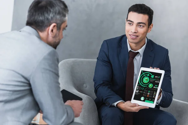 Lächelnder junger Geschäftsmann zeigt Kollegen digitales Tablet mit Geschäftsdiagrammen — Stockfoto